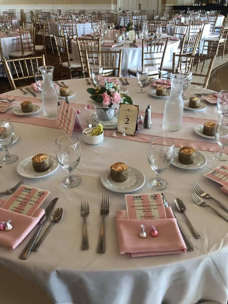Elegant luncheon table setting for the Aging Centenarian Luncheon, featuring pink and white decor, floral centerpiece, and dessert plates, reflecting ThompsonBaker's community support in St. Augustine.